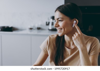 Close Up Smiling Happy Young Housewife Caucasain Woman 20s In Beige T-shirt Air Pods Headphones Talk By Video Call Listen To Music Cook Food In Light Kitchen At Home Healthy Diet Lifestyle Concept.