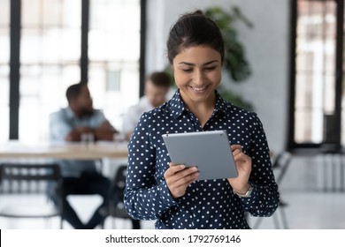 Close Up Smiling Indian Businesswoman Holding Digital Tablet, Standing In Modern Office Room, Employee Working Online, Using Apps, Writing Or Reading Email, Chatting In Social Network During Break