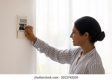 Close up smiling Indian using smart home system controller on wall, positive attractive young female switching temperature on thermostat or activating or turning off security alarm in apartment - Shutterstock ID 2013743105