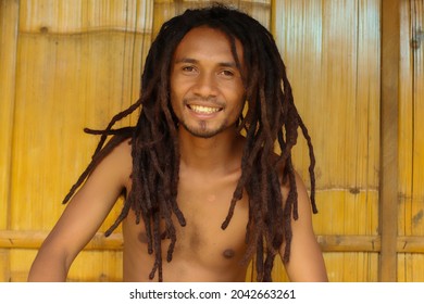 Close up of smiling indonesian guy man with dreadlocks with wooden in the background.