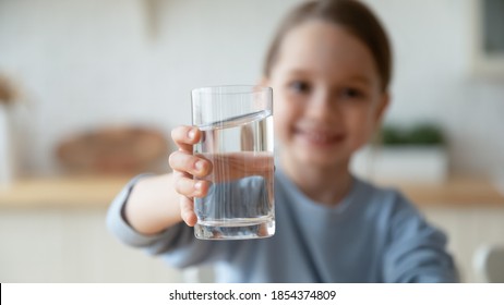 Close Up Smiling Little Girl Holding Glass Of Pure Mineral Water, Offering To Camera, Cute Pretty Child Kid Recommending Healthy Lifestyle Habit, Drinking Clean Aqua For Refreshment