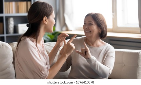 Close up smiling mature mother and grownup daughter speaking sign language, sitting on couch, young woman with elderly mum enjoying pleasant conversation, communicating, showing gestures, deaf family - Powered by Shutterstock