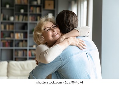 Close up smiling mature woman wearing glasses hugging adult son, standing in living room at home, family enjoying tender moment, beautiful happy middle aged woman embracing young man - Powered by Shutterstock