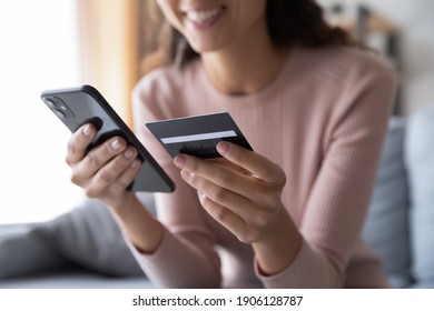 Close up smiling millennial woman holding smartphone and banking credit card, involved in online mobile shopping at home, happy female shopper purchasing goods or services in internet store. - Shutterstock ID 1906128787