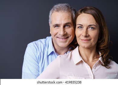 Close Up Of Smiling Older Couple Against A Blue Background And Wearing Business Casual Clothing