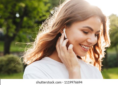 Close up of a smiling pretty young girl in wireless earphones outside