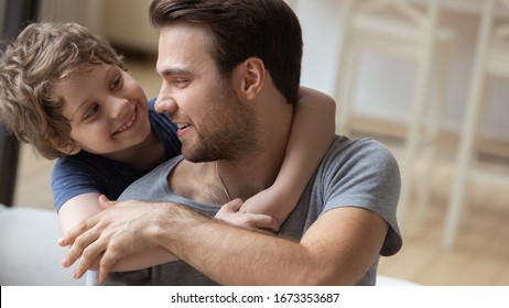 Close Up Of Smiling Small Preschooler Boy Child Piggyback Embrace Happy Young Dad Having Fun At Home Together, Loving Father And Little Son Hug Cuddle Enjoy Free Time Leisure Weekend Indoors