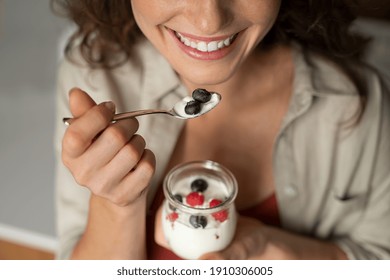 Close up of of smiling woman having a healthy breakfast at home with fruit and yogurt. Girl tasting yoghurt with blueberries and raspberries. Woman enjoy fresh yogurt for lunch, wellbeing diet concept - Powered by Shutterstock