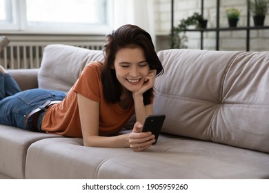 Close Up Smiling Woman Lying On Couch, Using Smartphone, Happy Young Female Spending Leisure Time With Gadget At Home, Looking At Phone Screen, Chatting Or Shopping Online, Browsing Device Apps