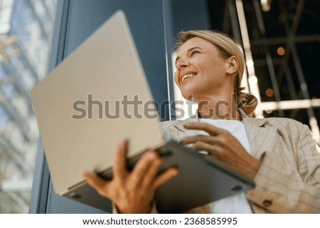 Close up of smiling woman manager working laptop on modern building background 