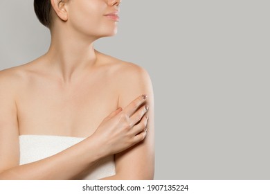 Close up of smiling woman touching soft skin on shoulder over grey background.  Beauty procedure, body cream advertisement concept. Cosmetic moisturizing lotion