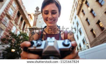 Close up of a smiling woman tourist taking photograph using a camera. Low angle shot of a woman taking photo outdoors with buildings in the background.