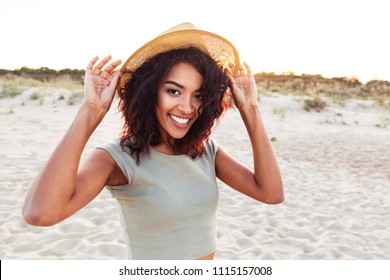 Close up of smiling young african girl in summer hat looking at camera at the beach
