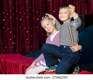 Close Up Smiling Young Boy And Girl Best Friend Performers Sitting On The Red Table At The Back Stage While Waiting For The Show To Begin.