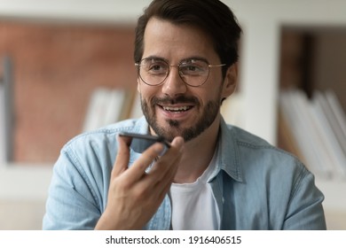 Close up of smiling young Caucasian man in glasses talk speak on smartphone on loudspeaker with client. Happy male employee record audio message, use digital voice assistant on cellphone gadget. - Shutterstock ID 1916406515