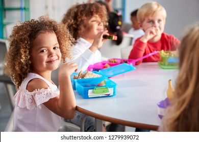 Close up of smiling young children sitting at a table eating their packed lunches together at infant school, girl smiling to camera, selective focus - Shutterstock ID 1279939072