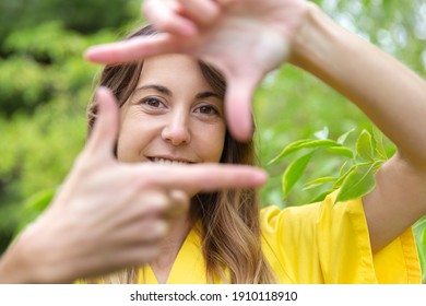 Close up of smiling young woman framing her face with her hands as a self-portrait. She is in nature. Space for text.
