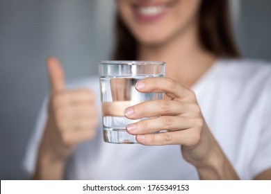 Close up of smiling young woman hold glass recommend drink clear still mineral water for body balance, happy female give recommendation for healthy lifestyle enjoying clean crystal aqua at home - Shutterstock ID 1765349153
