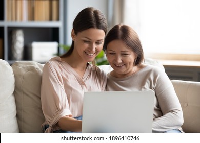 Close Up Smiling Young Woman With Mature Mother Using Laptop Together, Sitting Ojn Cozy Couch, Hugging, Enjoying Leisure Time, Older Mum And Grownup Daughter Surfing Internet Or Shopping Online