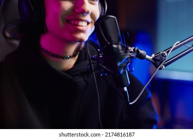 Close up of smiling young woman speaking to microphone in neon light while recording podcast or streaming gaming, copy space