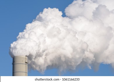 Close Up Of A Smokestack Of A Fossil Fuel Coal Power Plant With White Smoke Against A Completely Blue Sky And Lots Of Copy Space.