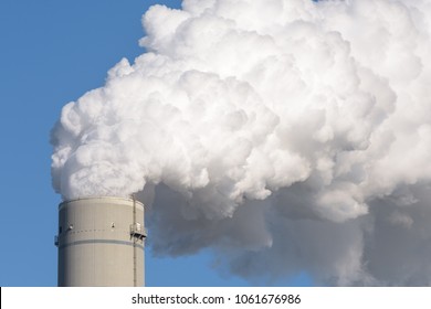 Close up of a smokestack of a fossil fuel coal power plant with white smoke against a completely blue sky and lots of copy space.