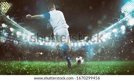 Close up of a soccer scene at night match with player in a white and blue uniform kicking the ball with power