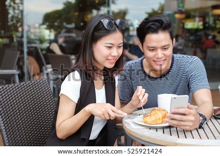 Close up soft focus on asian girl looking at smartphone and try to eat baked bakery,boy holding smart phone device for take a photo selfie concept.