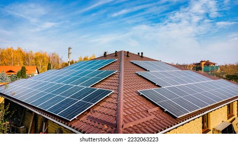 Close up of solar panels on roof home. The panels have the same beautiful blue color as the sky. from the attic level you can view the street with trees on the ground. - Shutterstock ID 2232063223