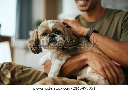 Close up of soldier cuddling his dog while relaxing at home. Dog is looking at camera.
