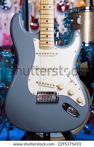 Close up of a solid sonic grey electric guitar with single coil pickups, white pickguard and silver hardware.