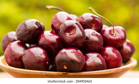Close up of some cherries in a wooden pot on a green and natural background