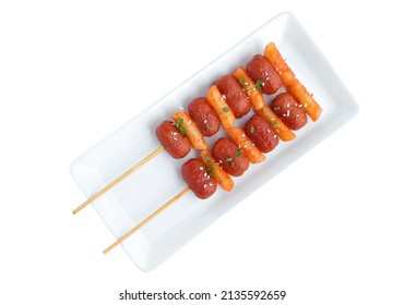 Close up of Sotteok, Skewered fried rice cakes and sausages topped with white sesame and green onion leaf on white plate with clipping path