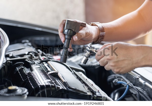 Close up\
spark plug coil in hand a man and use block wrench remove a bolt in\
service in garage and engine room \
background
