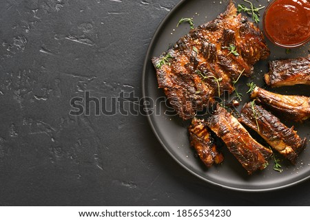 Close up of spicy grilled spare ribs on plate over dark stone background with copy space. Top view, flat lay