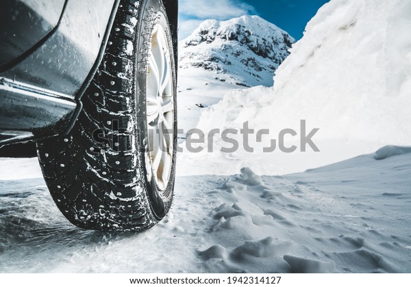 Close up of a spiked winter tire with\
a snow covered road and mountains in the\
background.