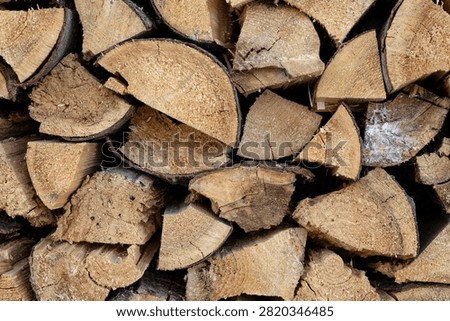 Close up of split firewood stacked together, showing natural wood grain, bark texture and freshly cut surfaces.