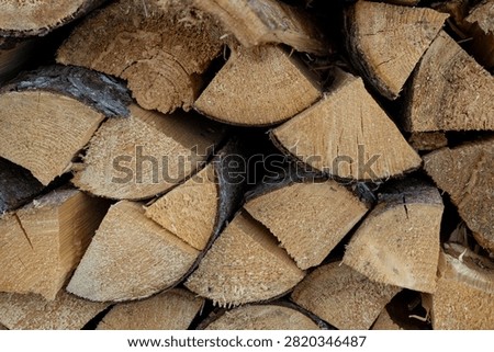 Close up of split firewood stacked together, showing natural wood grain, bark texture and freshly cut surfaces.