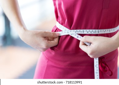 Close up Sport woman measuring her waist by using waistline or tape, comparing her waist size before and after workout for firming body, diet with accessory equipment in gym - Healthcare concept
