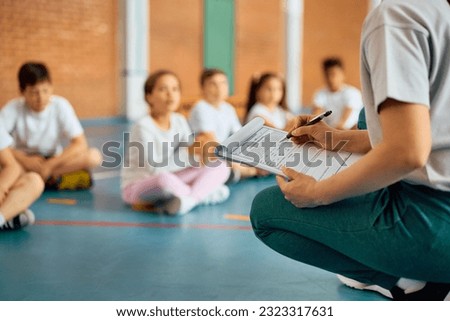Close up of sports teacher taking notes during physical education class at school gym.
