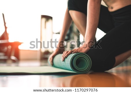 Close up of sporty woman folding yoga mattress in sport fitness gym training center background. 