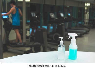 Close Up Spray Bottle Of Blue Disinfectant And Alcohol Gel With Blurred Background Of Asian Man Workout In Gym. Concept For Prevention And Protection Of Corona Virus Covid 19 In Fitness Center.