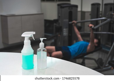 Close Up Spray Bottle Of Blue Disinfectant And Alcohol Gel With Blurred Background Of Asian Man Workout In Gym. Concept For Prevention And Protection Of Corona Virus Covid 19 In Fitness Center.