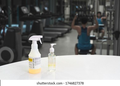 Close Up Spray Bottle Of Yellow Disinfectant And Alcohol Gel With Blurred Background Of Asian Man Workout In Gym. Concept For Prevention And Protection Of Corona Virus Covid 19 In Fitness Center.