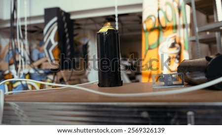 Close up of spray cans in empty basement with graffiti drawings on walls. Focus on paint cans with underground warehouse used as crime haven by hooligans in blurry background