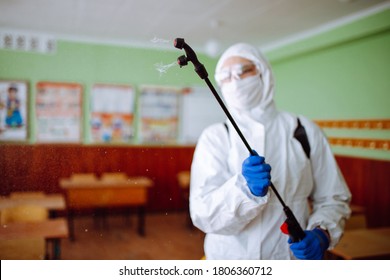 Close up of a spray with sanitizing liquid in the hands of a man wearing a protective suit in the schoold classroom. Disinfectant sterilizes the auditorium before the studing process begins. Covid-19.