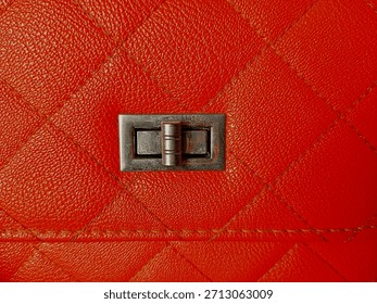 Close up of square or box pattern on orange bag with flap showing lock button with space for text.