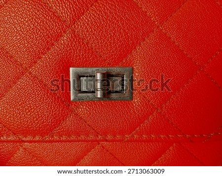 Close up of square or box pattern on orange bag with flap showing lock button with space for text.
