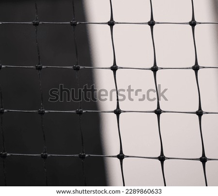 close up of squares on plastic fence against white and black background of wall shadows and shapes in back geometric shapes squares lines and angles textured shaped background backdrop fence wallpaper
