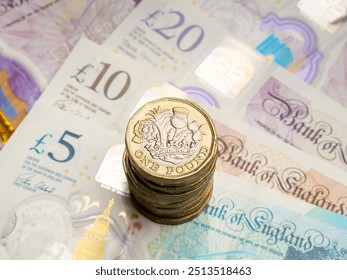 Close up of stack of British pound coins resting on pound notes money cash, UK